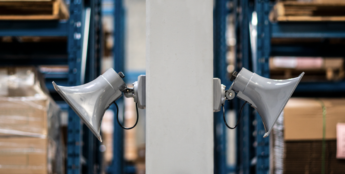 Two Algo IP horn speakers mounted on a pillar in an industrial warehouse.